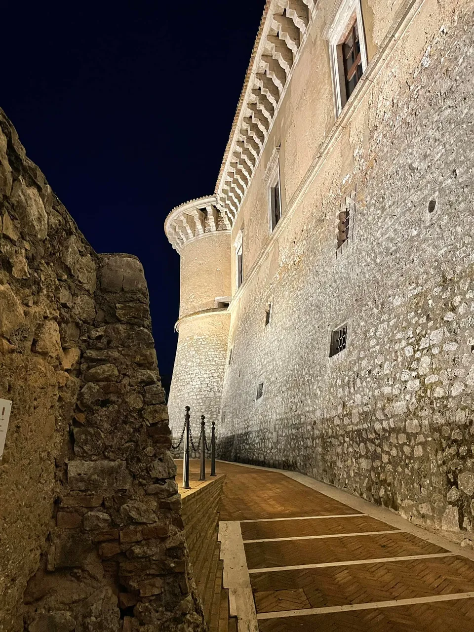 Le mura in pietra del Castello di Alviano illuminate di notte, viste dal basso lungo una rampa