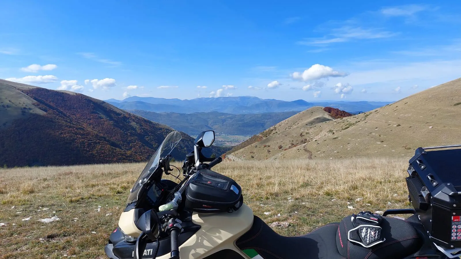 Una moto parcheggiata su un altopiano erboso, con montagne e cielo azzurro sullo sfondo