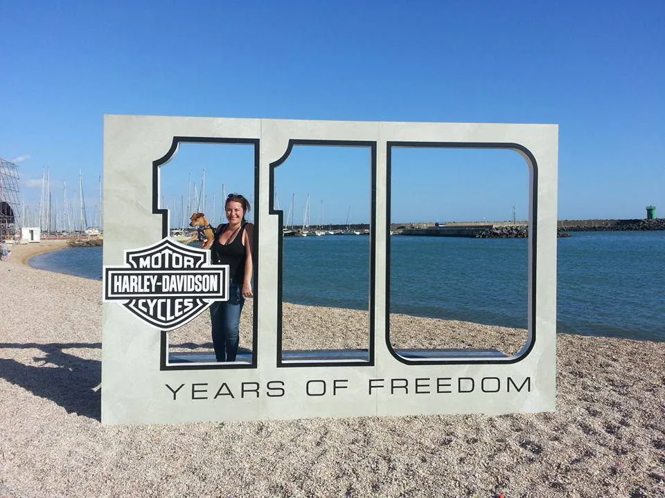 Una donna davanti alla grande scritta «110 Years of Freedom» di Harley-Davidson, su una spiaggia