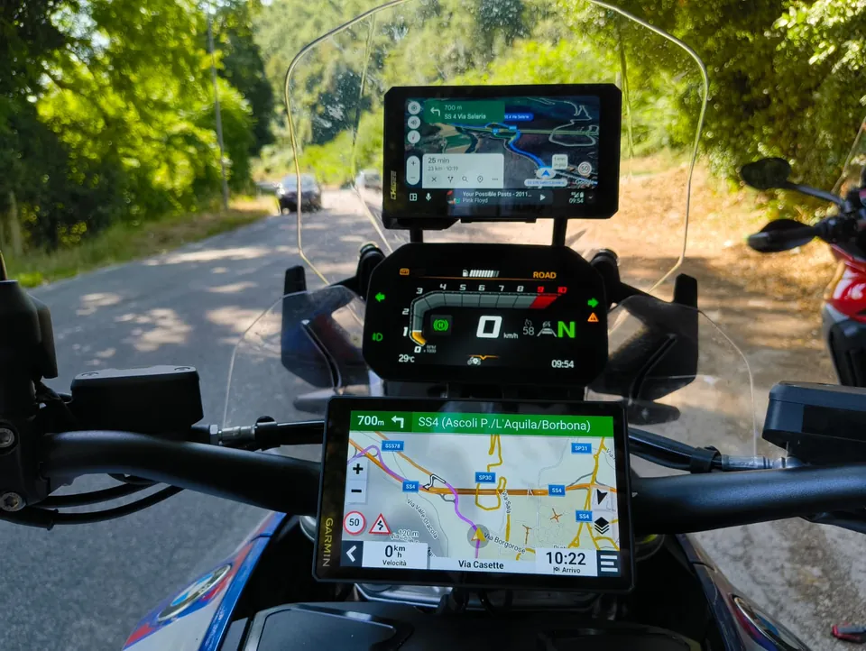 Il manubrio di una moto con cruscotto, navigatore Garmin e smartphone montati, su una strada di campagna