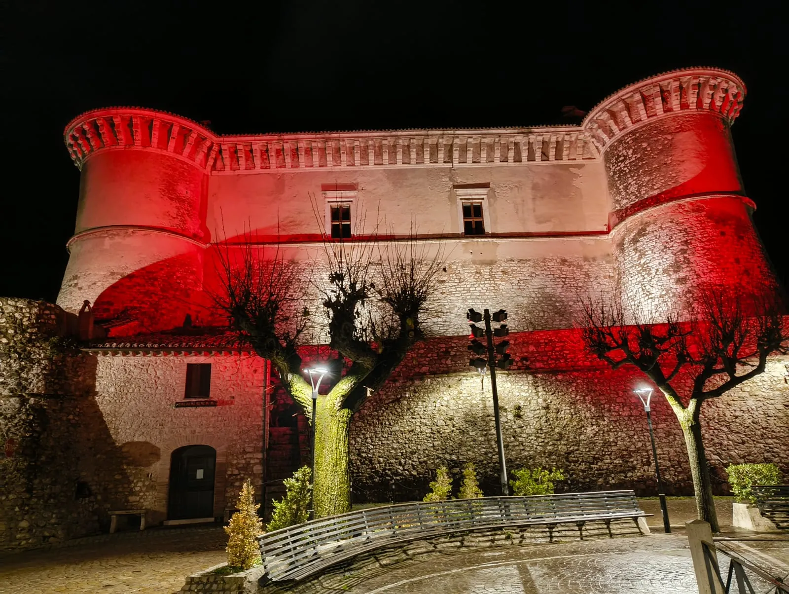 Il Castello di Alviano di notte, con torri e facciata illuminate di rosso e bianco e la piazza alberata