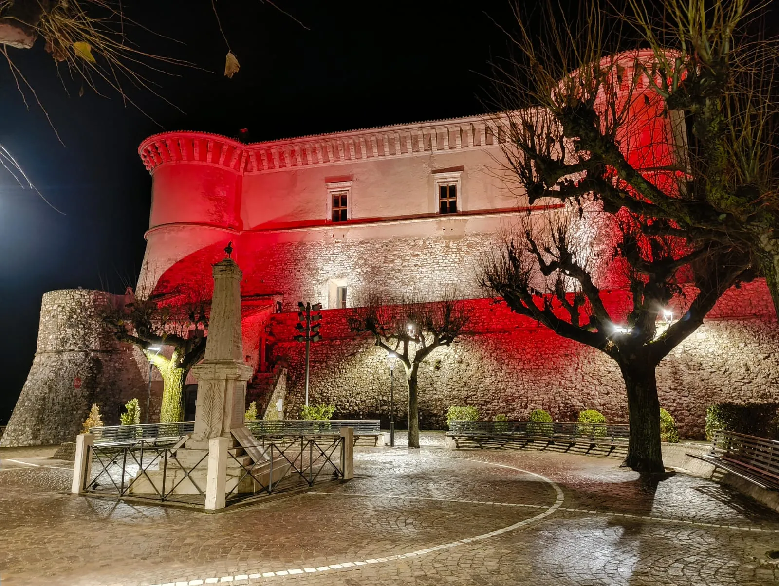 La piazza del Castello di Alviano di notte, con il monumento al centro e la rocca illuminata di rosso